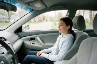 Jeune adolescente assise sur le siège avant passager d'une voiture familiale, ceinture de sécurité attachée, regardant par la fenêtre