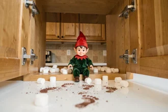 Lutin farceur perché dans un placard de cuisine entouré de chamallows éparpillés et d'empreintes en poudre de cacao sur le plan de travail